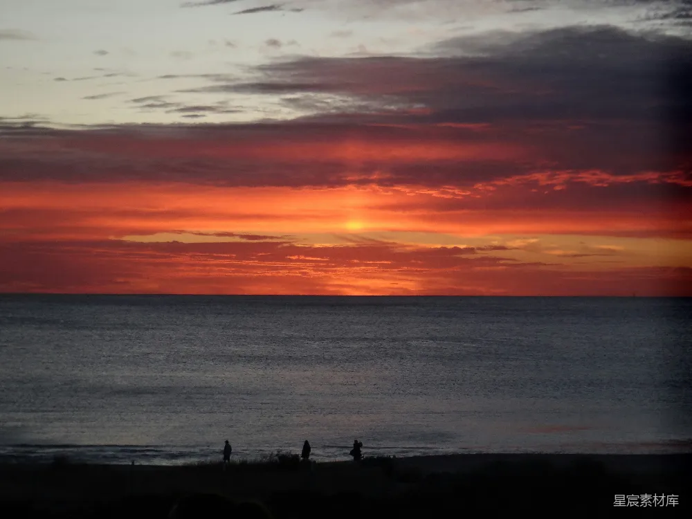高清摄影  夕阳映照在海面上，人们在海滩上散步