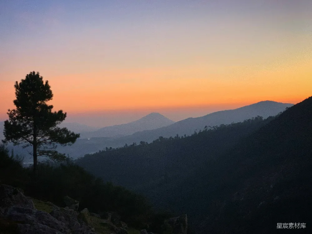 高清摄影  一棵孤独的树在群山之上绚丽的夕阳映衬下剪影。