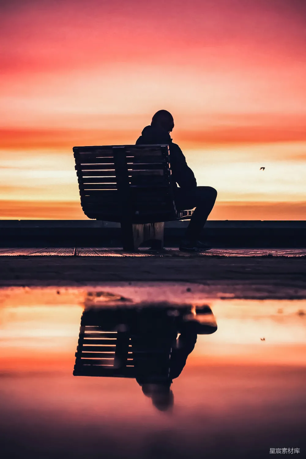 高清摄影  一个男人在海滩附近的长椅上坐着的剪影，夕阳西下。