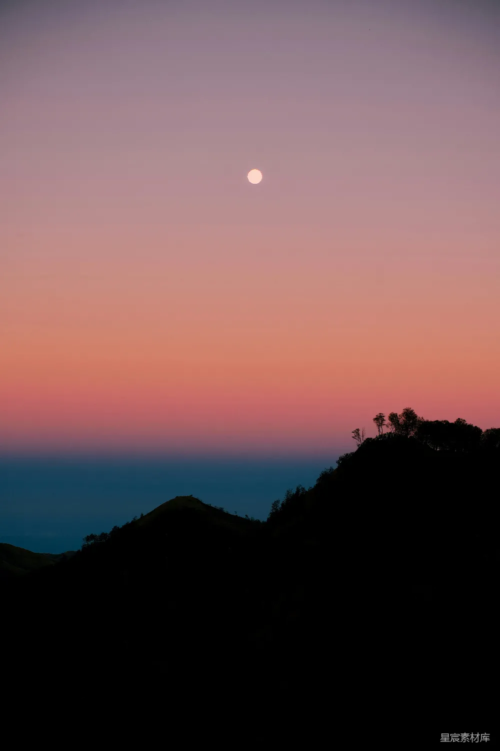 高清摄影  明月高挂于暗色的山峦之上，天空中有一片绚丽的夕阳。