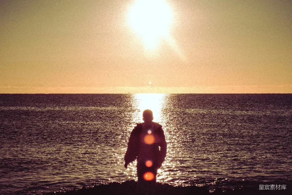 高清摄影  穿着黑色潜水服的男人站在海滩上，夕阳西下。
