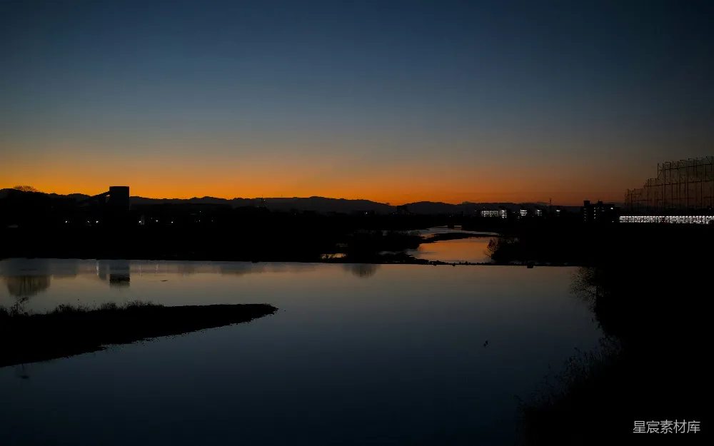 高清摄影 自然 夕阳的余晖洒在平静的河面上，远处的城市天际线清晰可见。