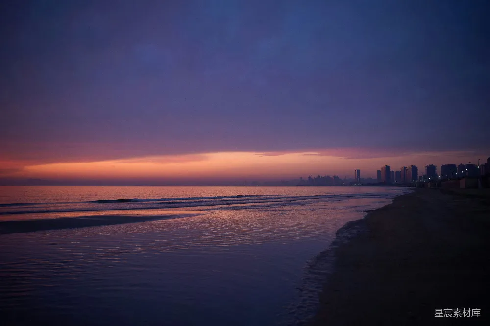 高清摄影  海滩上的日落景色，背景中有建筑物。
