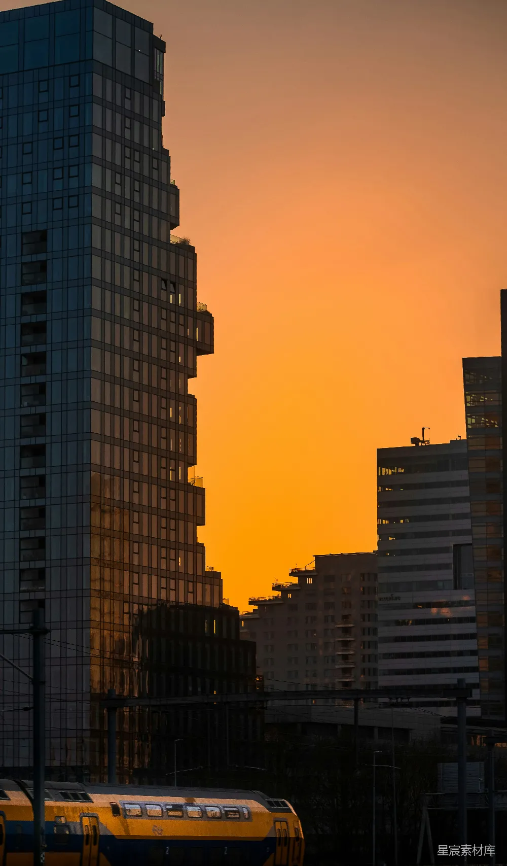 高清摄影  一列黄色的火车在夕阳下穿过高楼大厦。