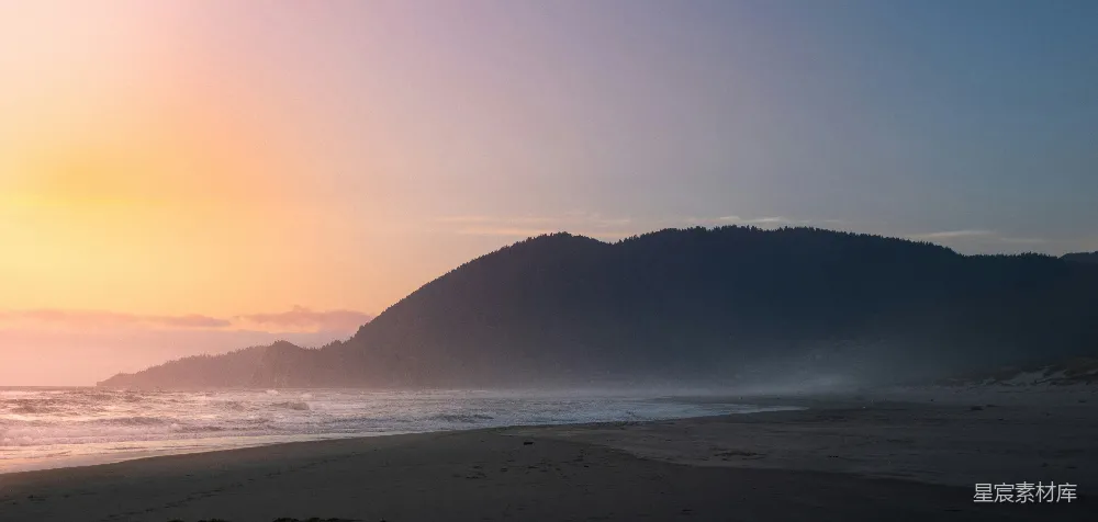 高清摄影  太阳正落在这片海滩上，背景是连绵的山脉。
