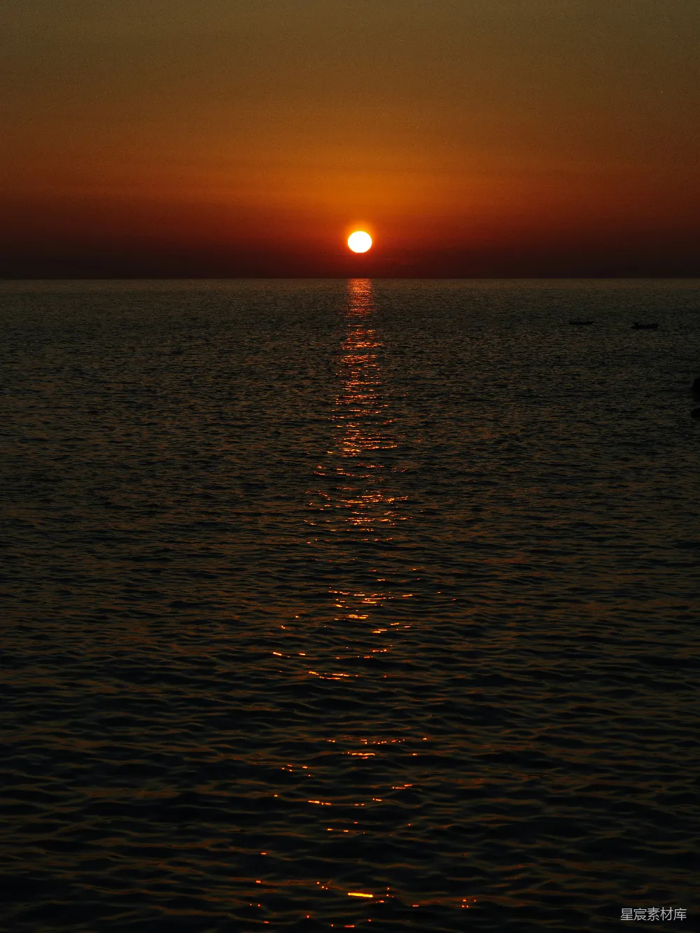高清摄影  夕阳正从海面落下，一艘小船在水中漂浮。