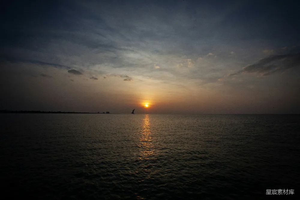 高清摄影  夕阳正缓缓落下，海面上一艘帆船在远处漂浮。
