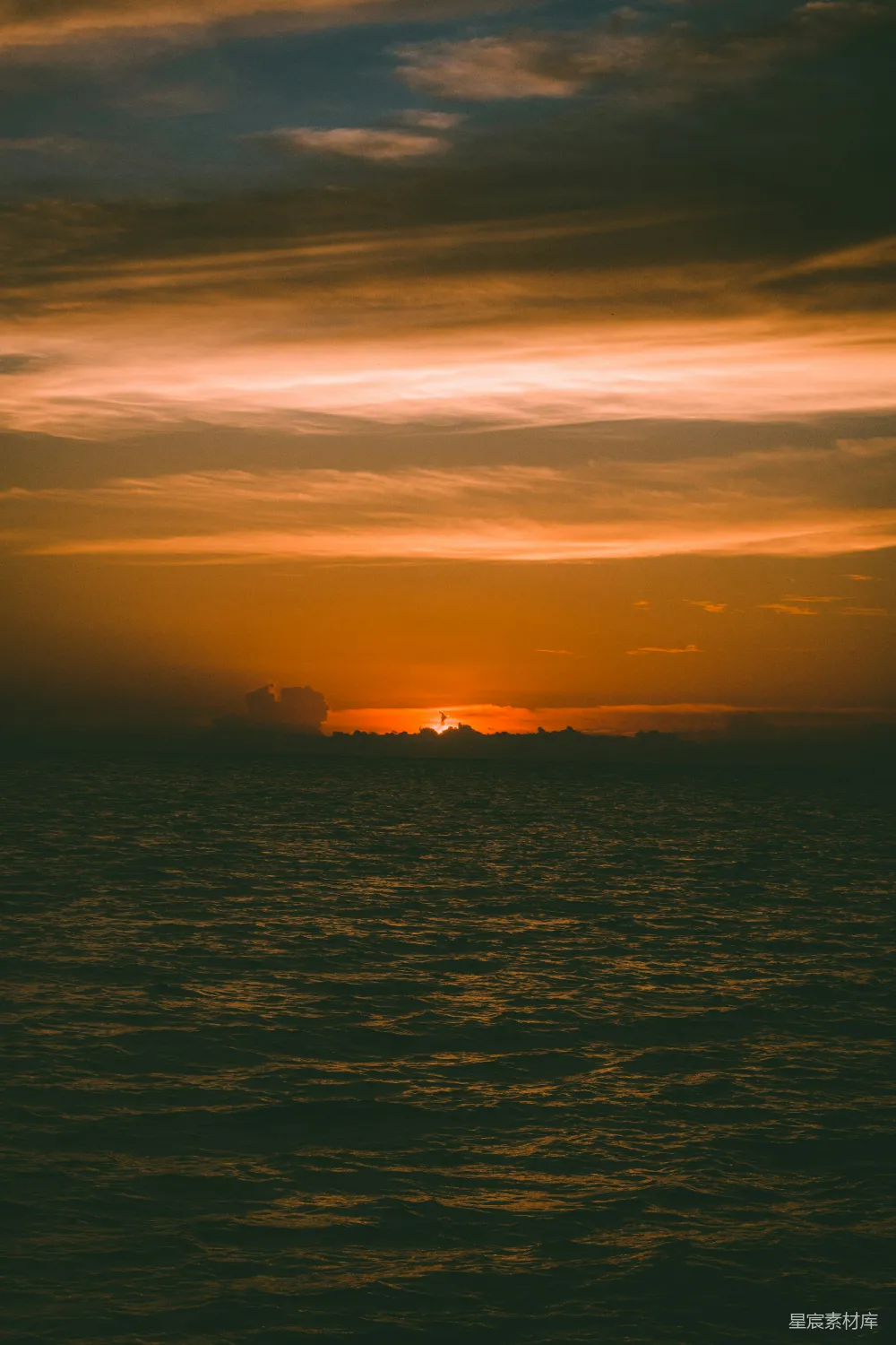 高清摄影  在多云的天气里，夕阳正缓缓落下，映照着海洋。