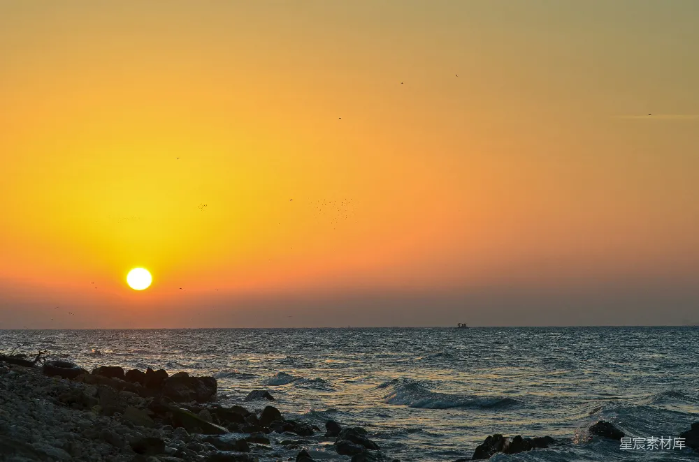 高清摄影  夕阳映照在海面上，远处有一艘船。
