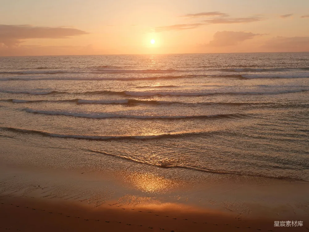 高清摄影  金色的夕阳照耀着平静的海浪和沙滩。