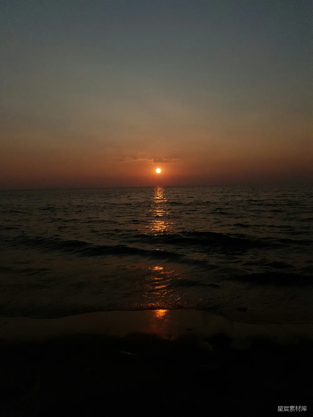 高清摄影  夕阳正缓缓沉落在海滩上的水面上。