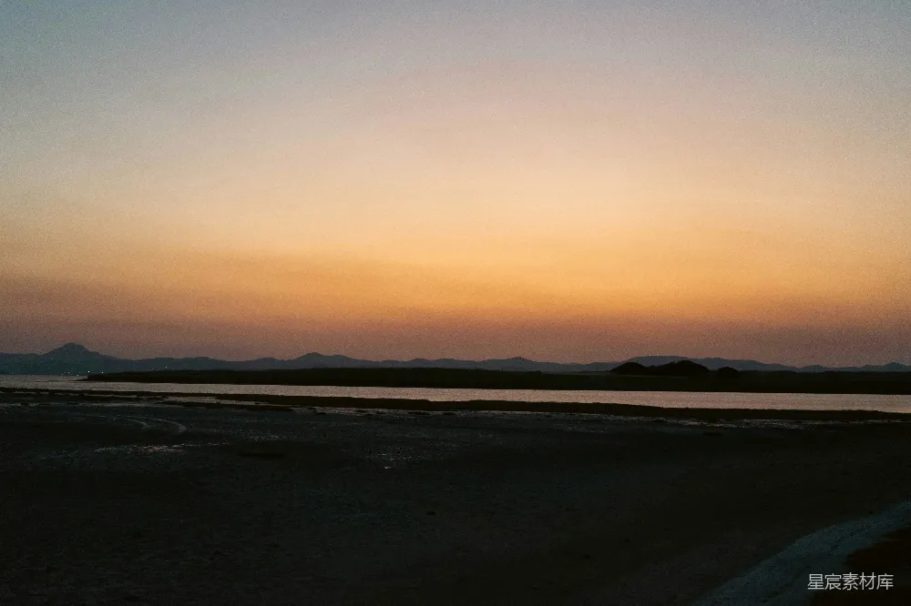 高清摄影  夕阳映照在水面上，背景中有连绵的山脉。