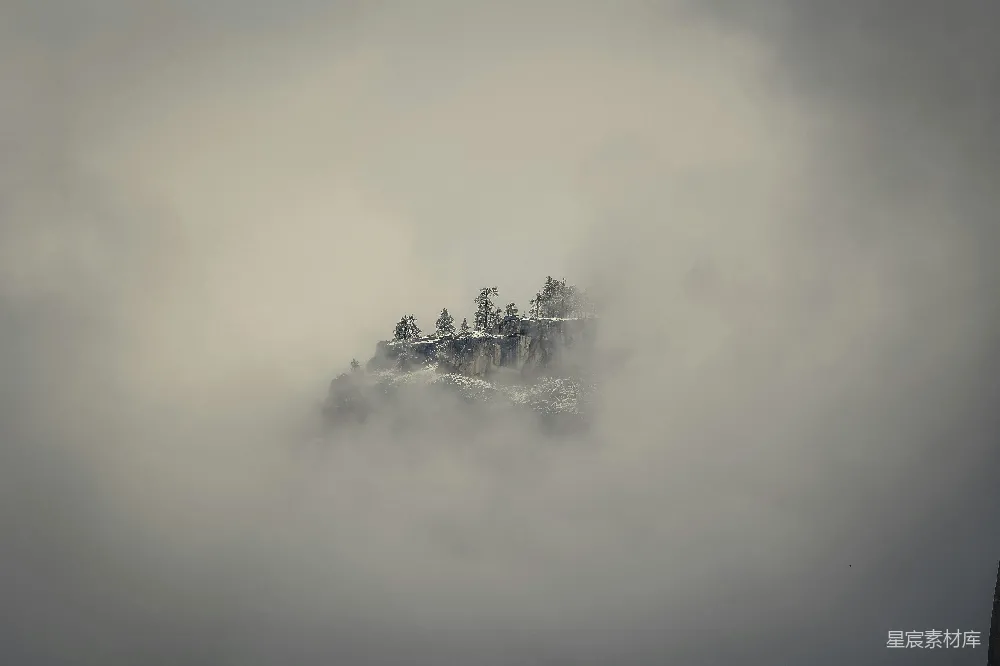 高清摄影  一座被雾气笼罩的山，山顶上长着树木。