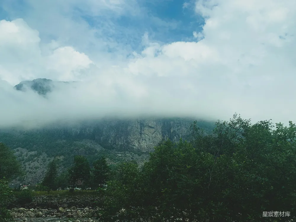 高清摄影 旅行 自然 一座山峰被云雾和树木覆盖，在蓝天的映衬下。
