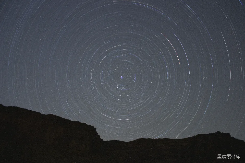 高清摄影  星星在夜空中穿过，形成围绕岩石剪影的同心圆。
