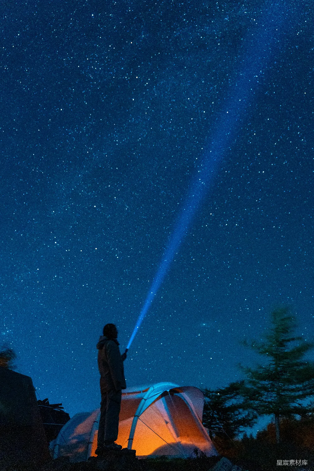 高清摄影  露营者手持手电筒照亮上方星空，帐篷在光芒中闪烁。