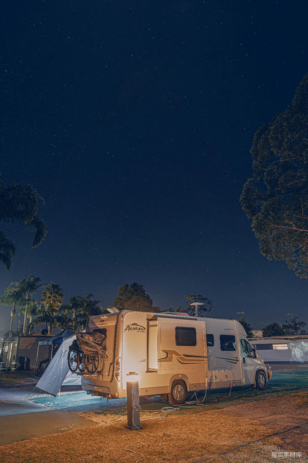 高清摄影  夜晚，一辆露营车停在树旁。