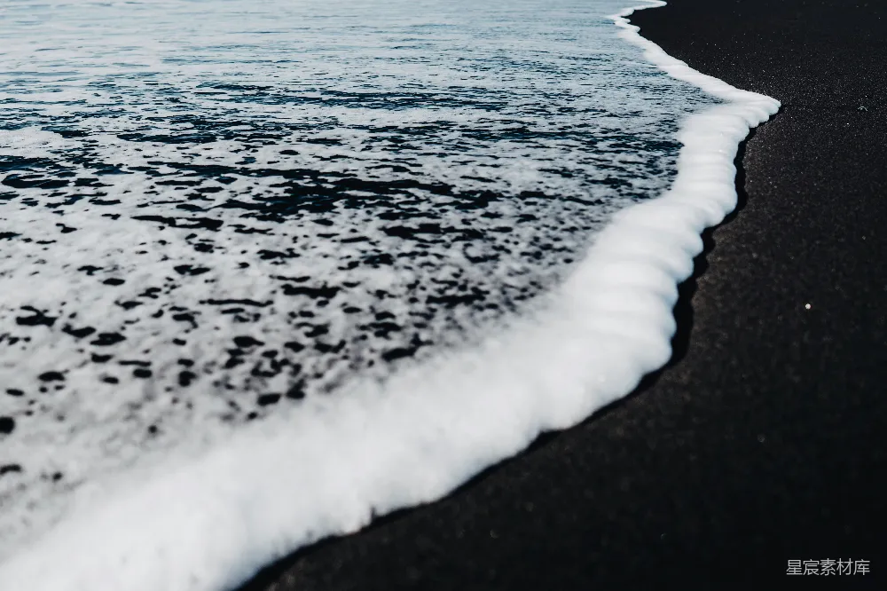 高清摄影  一片黑色的沙滩，海浪拍打着海岸。