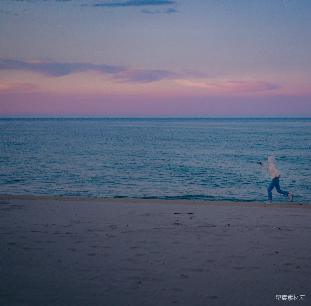 高清摄影  穿着白色连衣裙的女人在夕阳下走在海滩上