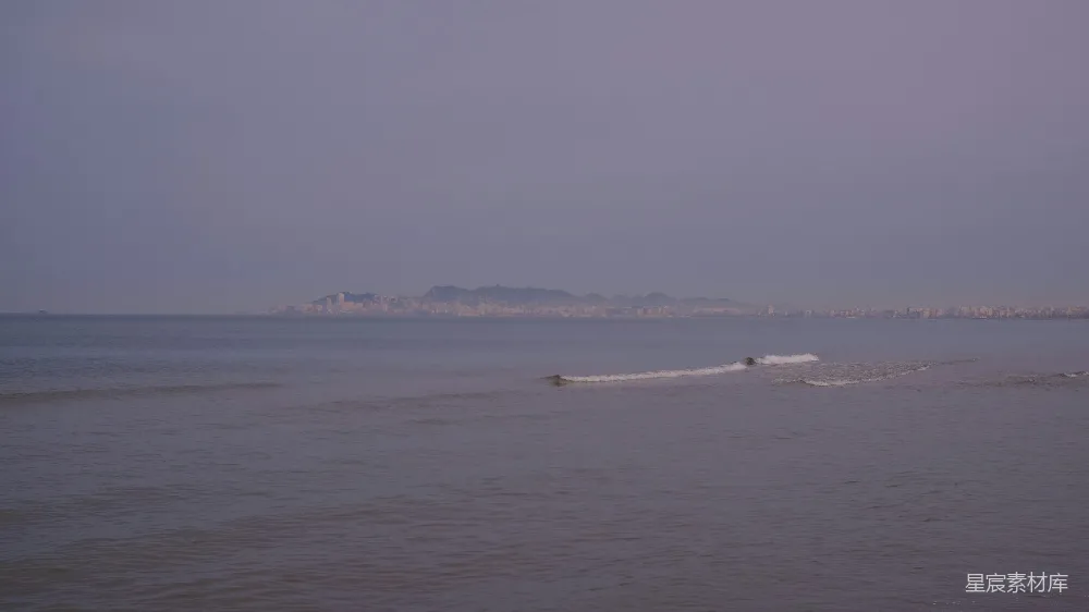 高清摄影  平静的海洋与远处朦胧的天际下城市景观