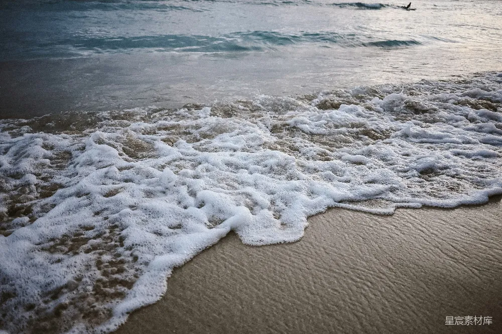 高清摄影  海浪拍打着沙滩，白色的泡沫轻轻拂过。