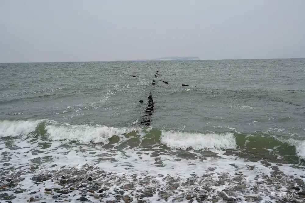 高清摄影  海浪拍打着岩石海岸，木桩立在岸边。