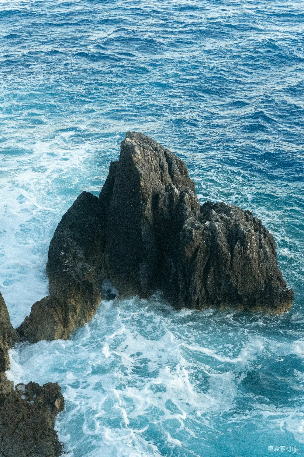 高清摄影  海洋中的尖锐岩石，海浪拍打在岩石上。