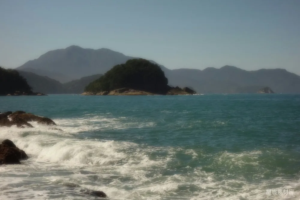 高清摄影  海浪拍打着岩石海岸，远处是岛屿和山脉。