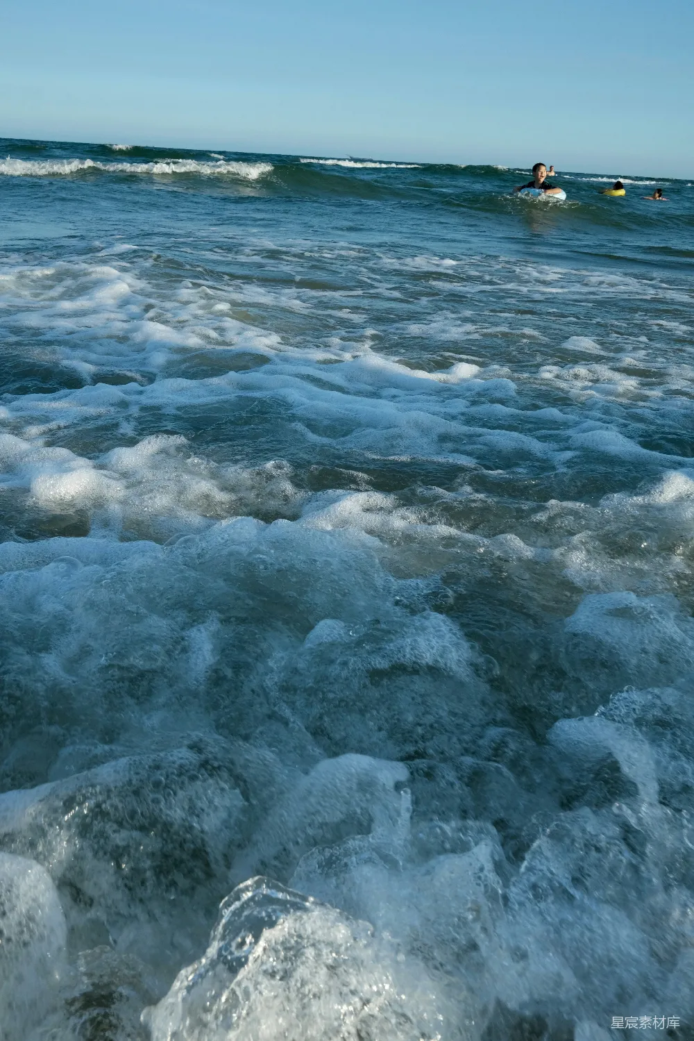高清摄影  海浪拍打着沙质海滩，冲浪者在其中冲浪。