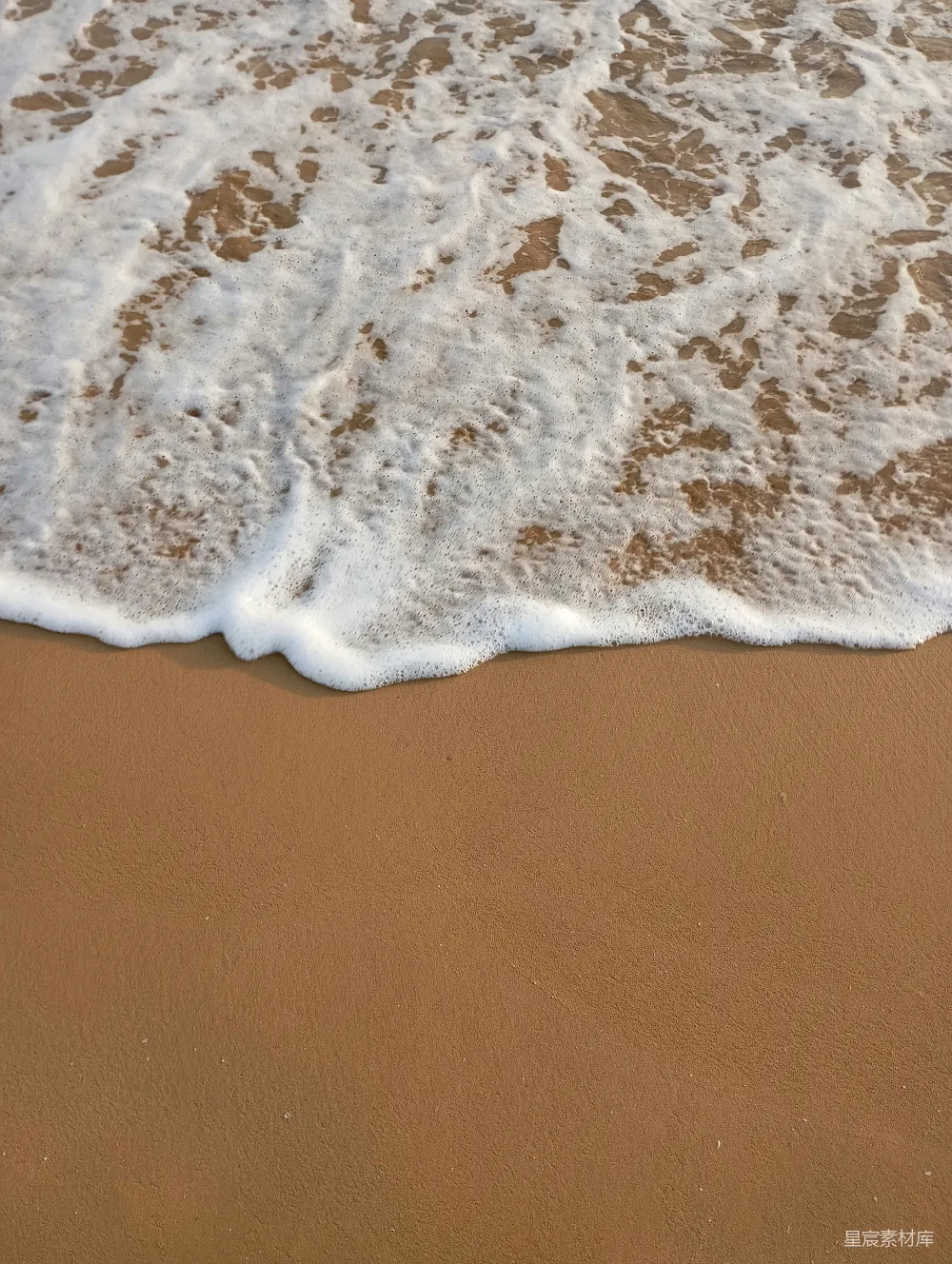 高清摄影  白色的泡沫浪花拍打着海滩上的棕色沙子。