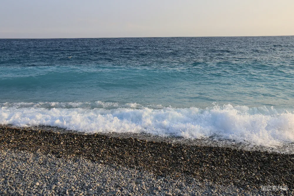 高清摄影  海浪轻柔地拍打着晴空下的一片鹅卵石海滩。