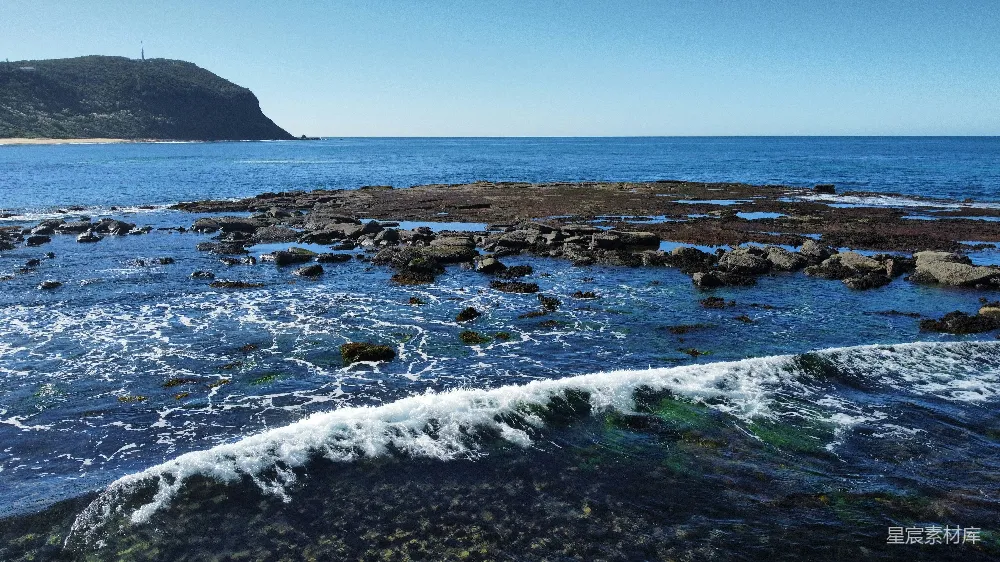 高清摄影  海浪拍打着岩石海岸，远处有一座海岬。
