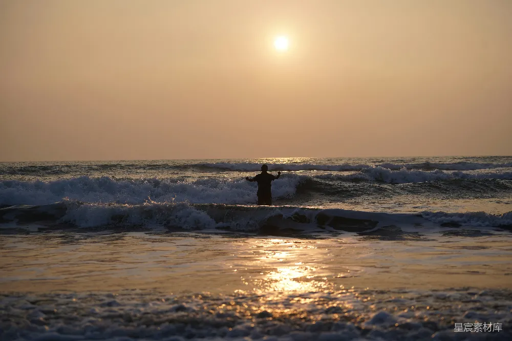 高清摄影  站在夕阳下的海里的人