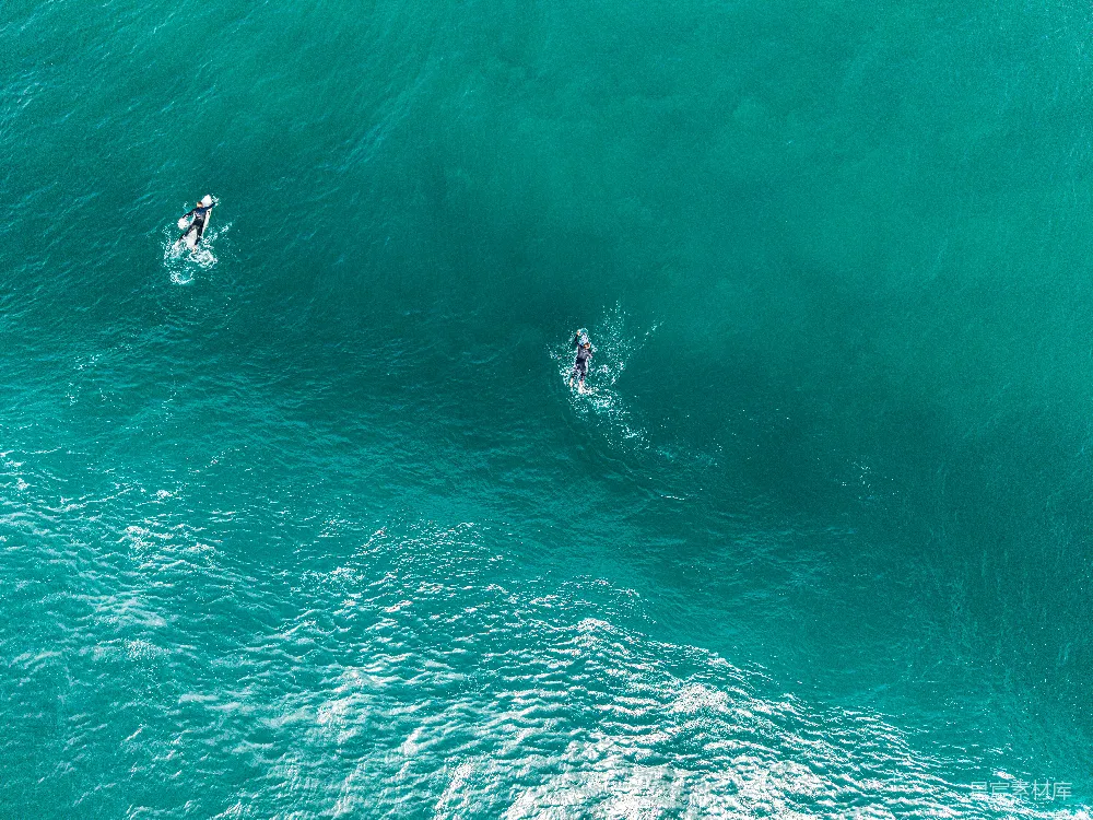 高清摄影  两名冲浪者在碧蓝色的海水中，伴随着波浪。