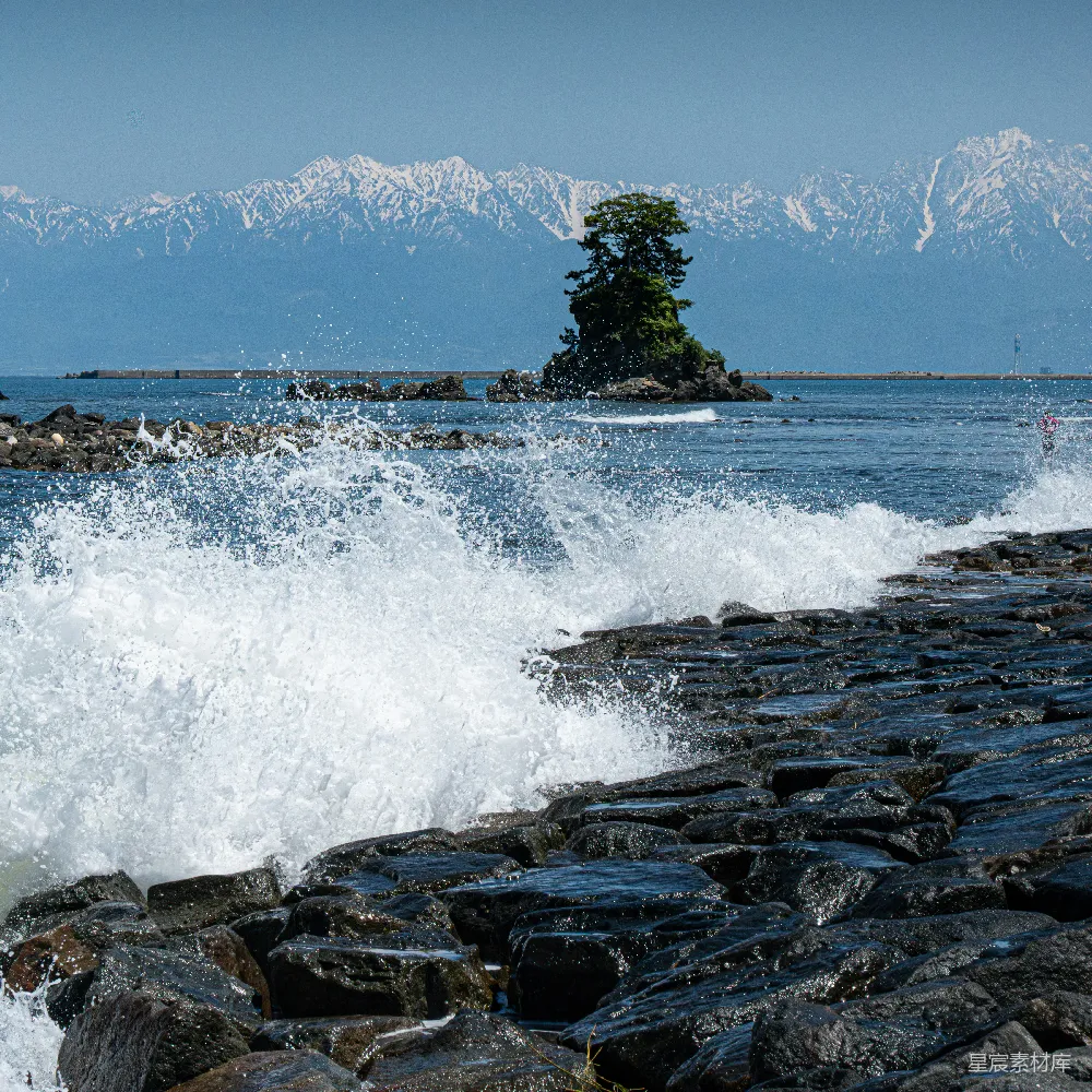 高清摄影  海浪拍打着岩石岸边，远处的雪山矗立。