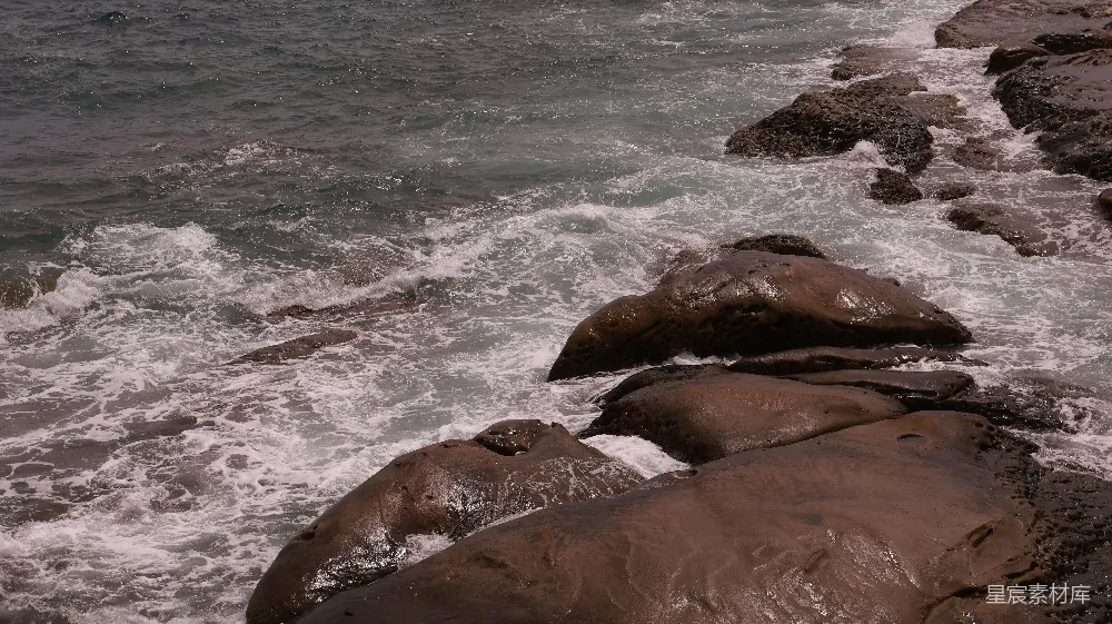 高清摄影  海浪拍打着海岸边湿漉漉的黑岩石。