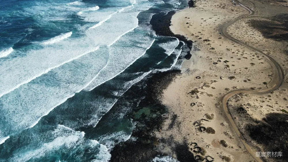 高清摄影  海浪拍打着沙滩，蜿蜒的道路延伸其间。