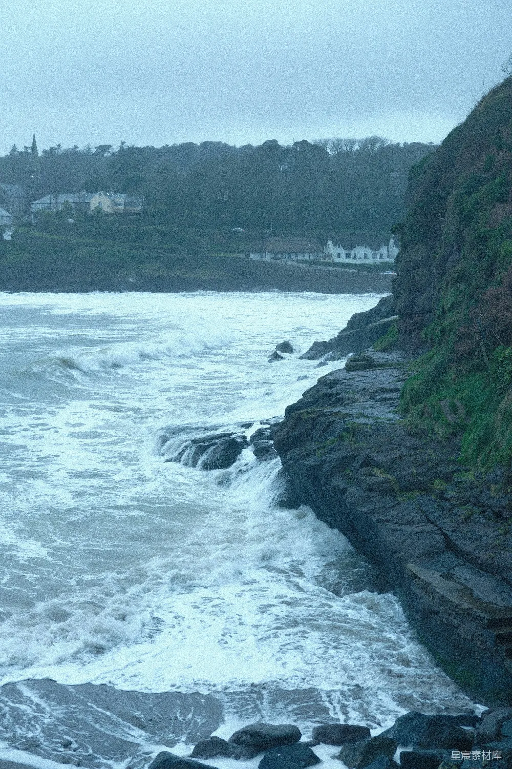 高清摄影  海浪拍打着岩石海岸，背景中有沿海村庄。