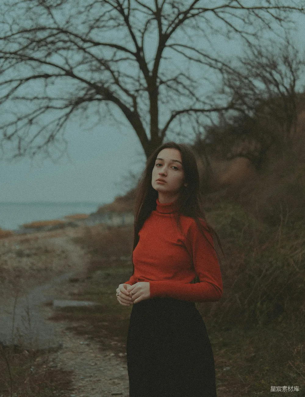高清摄影  一个穿着红色上衣的女人站在一棵树旁边。