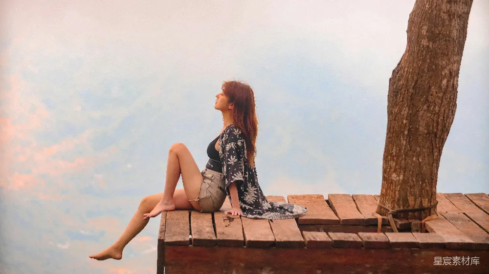 高清摄影  一个女人坐在树旁的木码头上。
