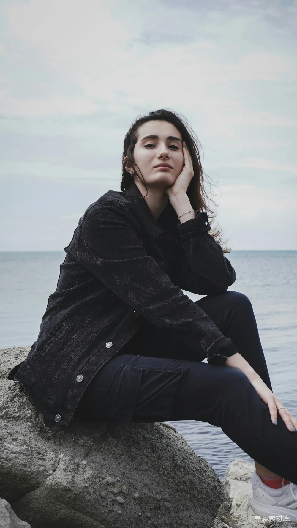 高清摄影  穿着黑色外套的女人坐在海边的岩石上，白天。