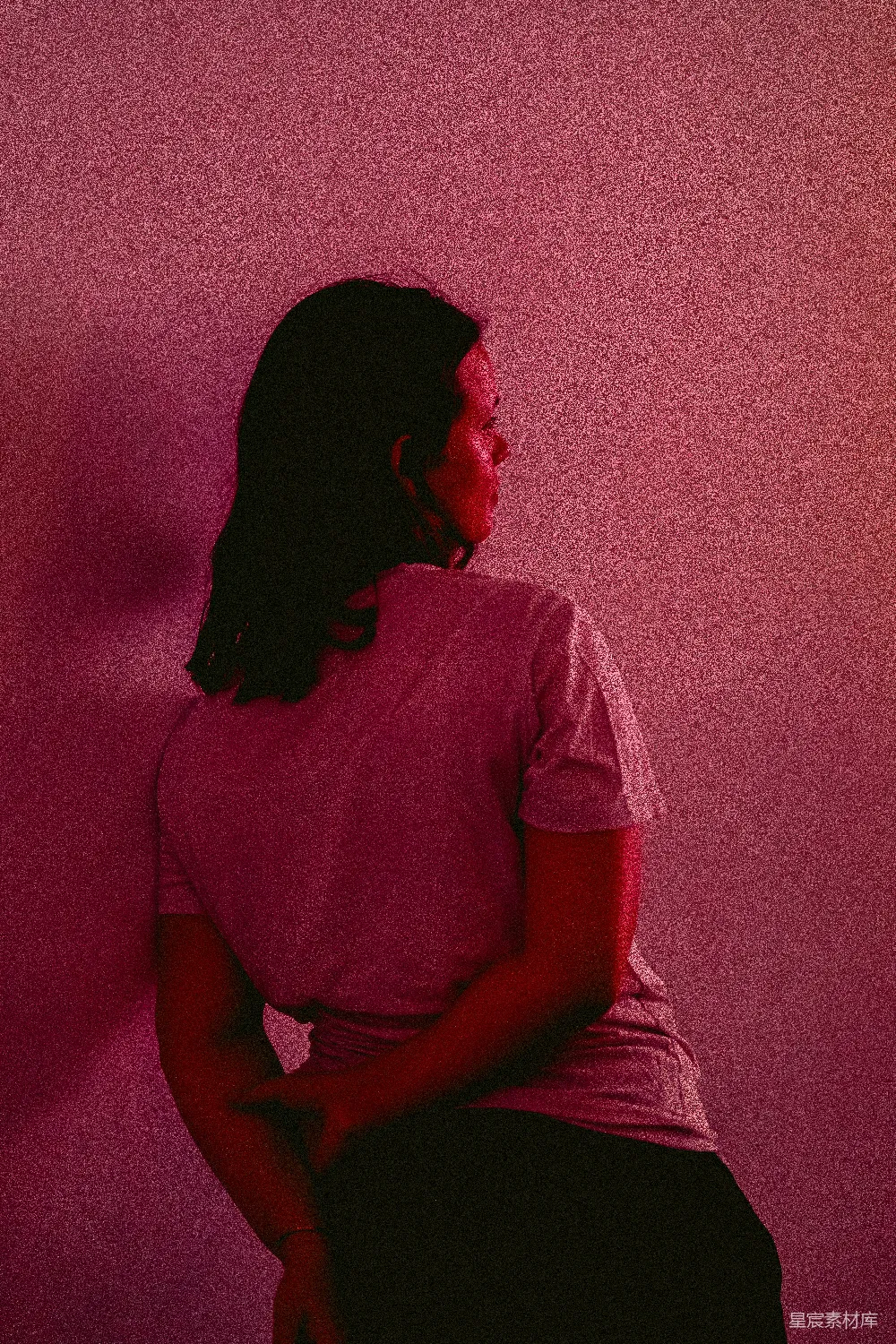 高清摄影 人物 一个女人坐在粉红色墙前的凳子上。