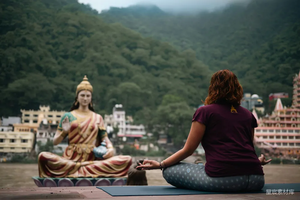 高清摄影  一位女士坐在瑜伽垫上，面前有一尊佛像。