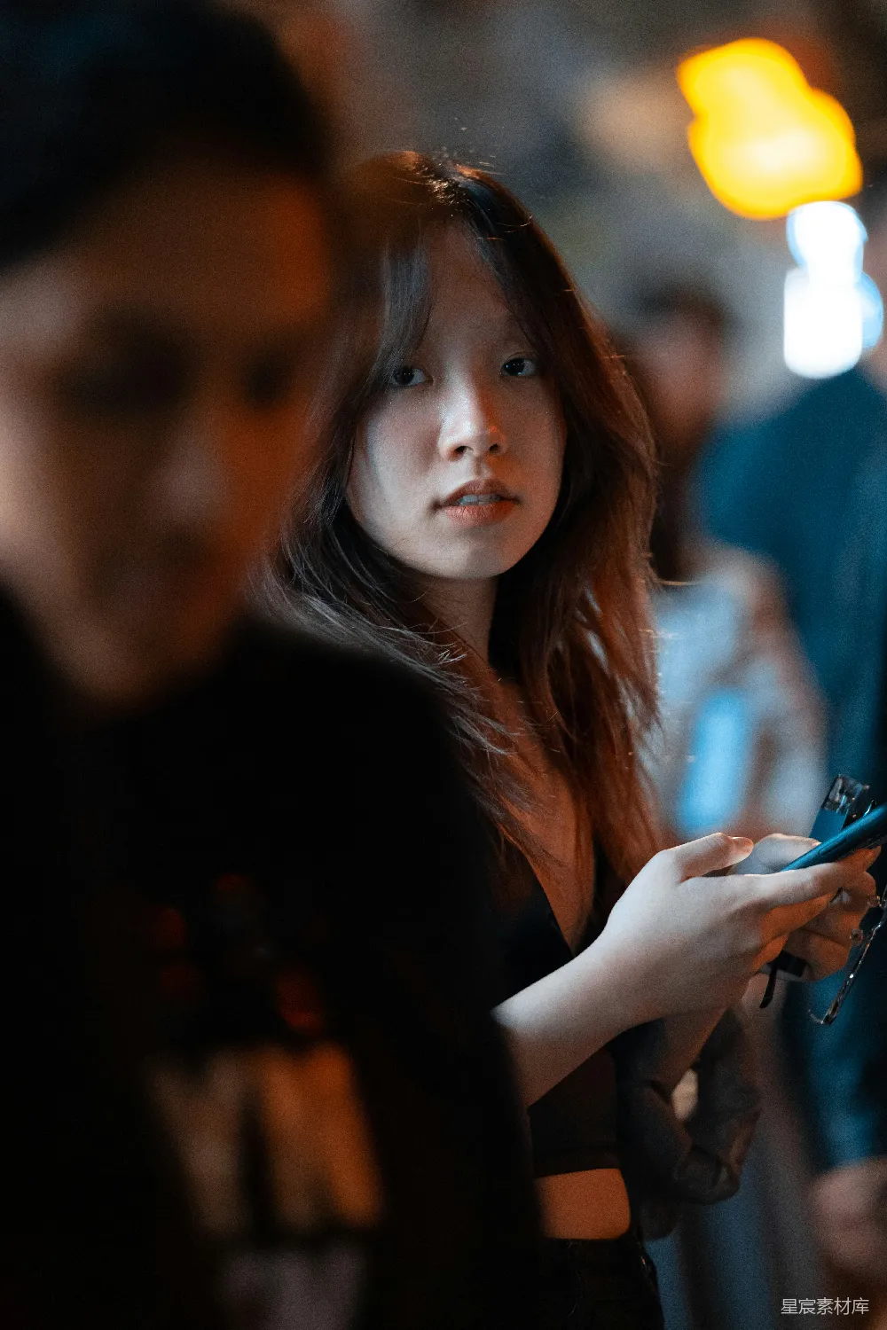高清摄影  一个女人站在一个拿着手机的男人旁边。