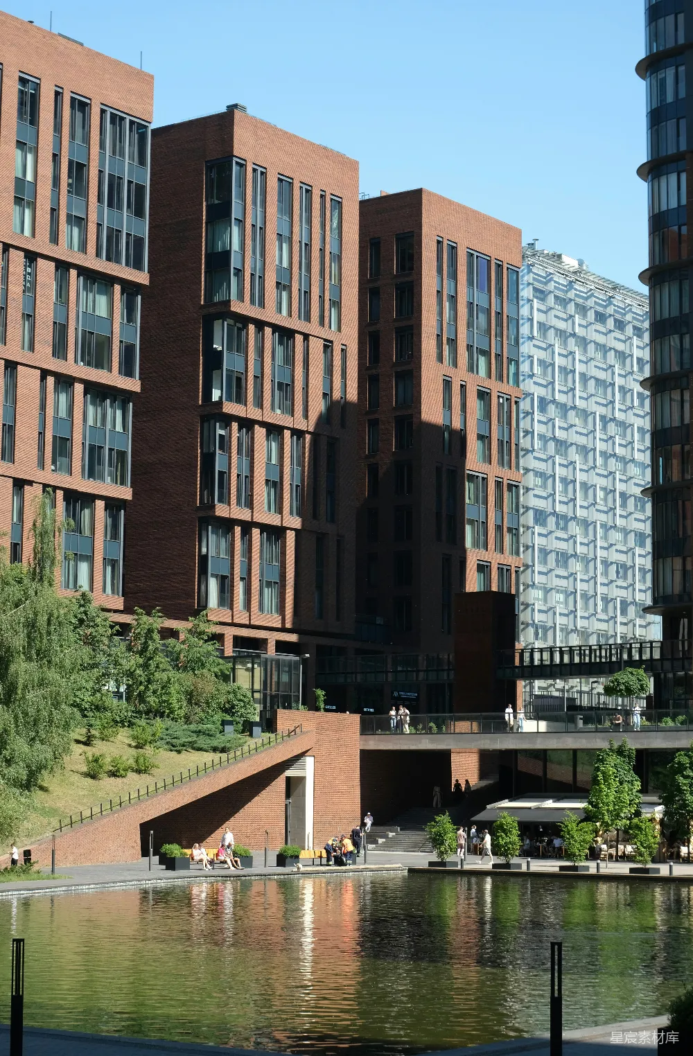 高清摄影  现代砖砌建筑倒映在水中，周围有人和树木。