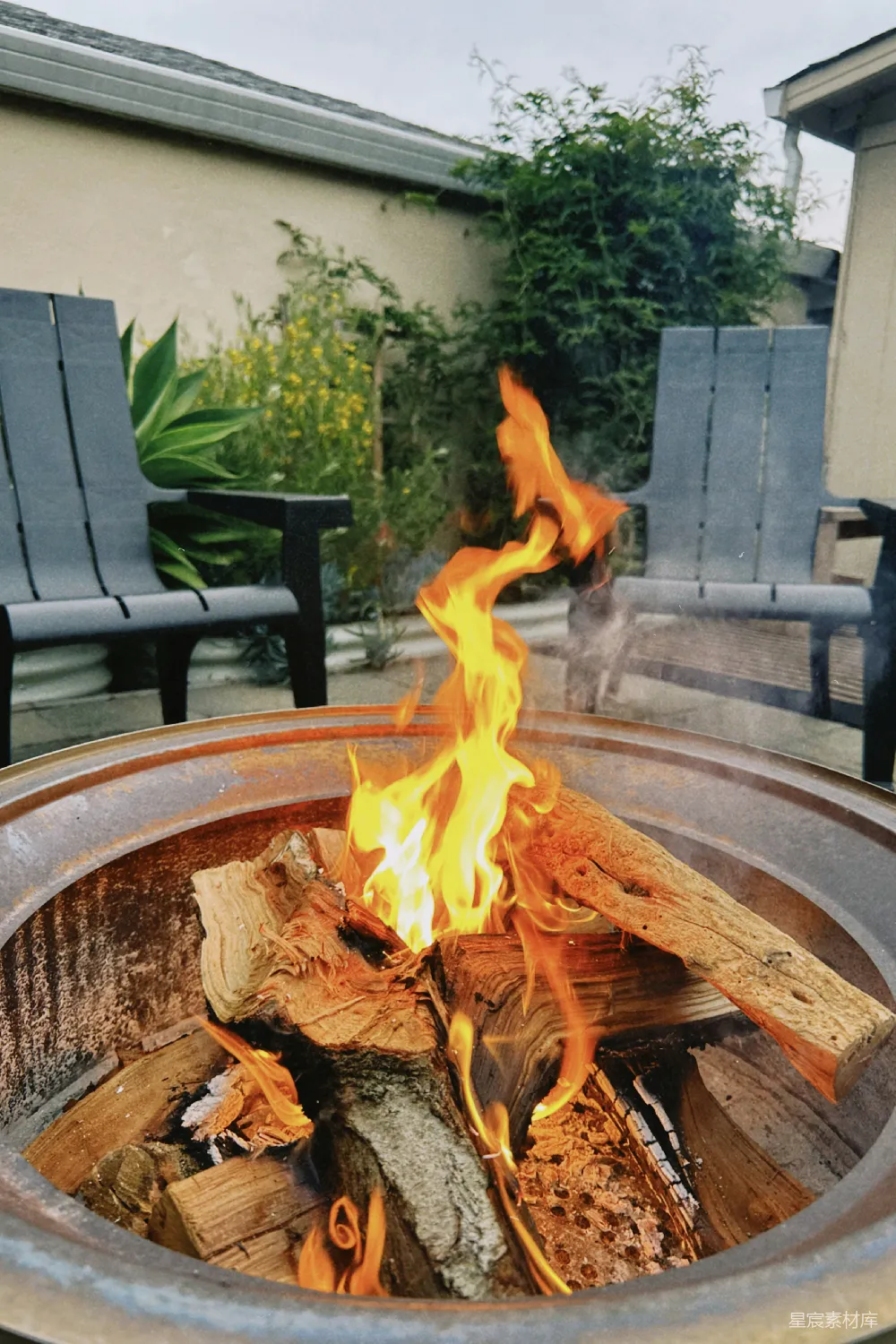 高清摄影  一个后院的篝火坑，里面燃烧着木头，旁边放着两把椅子。