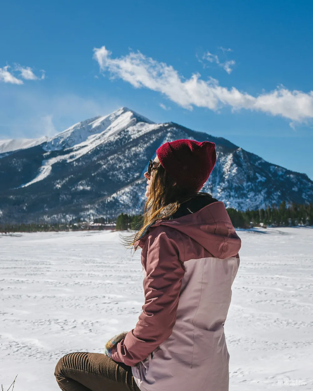 高清摄影  一位女士坐在雪地里，背景是山。