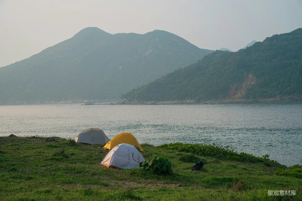 高清摄影 旅行 在沿海的小山上搭建露营帐篷，周围是山脉和大海。