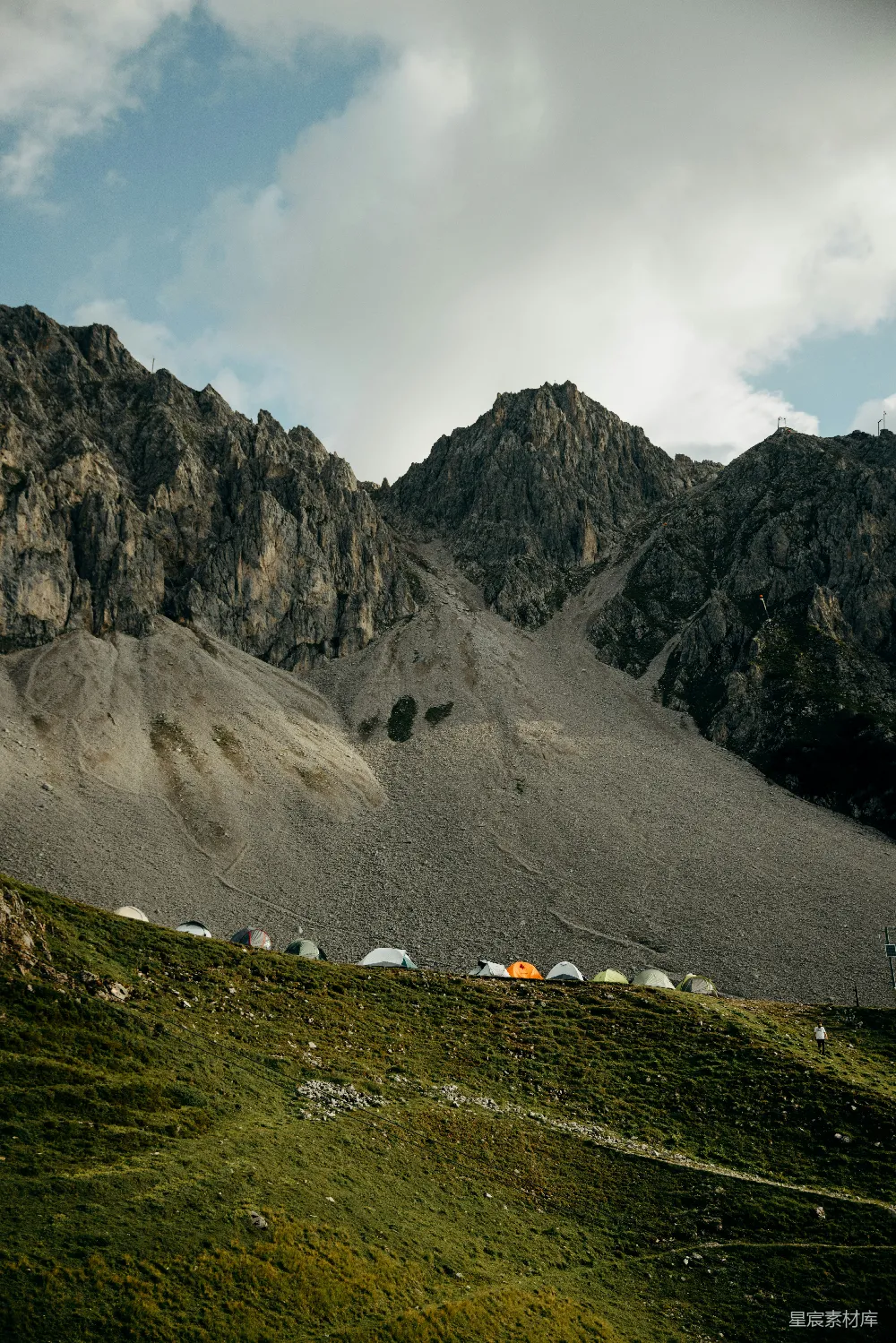 高清摄影  帐篷沿着草地山丘排列，背景是岩石山峰。
