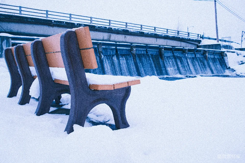 高清摄影  冬日覆盖着积雪的公园长椅，旁边有一座桥。